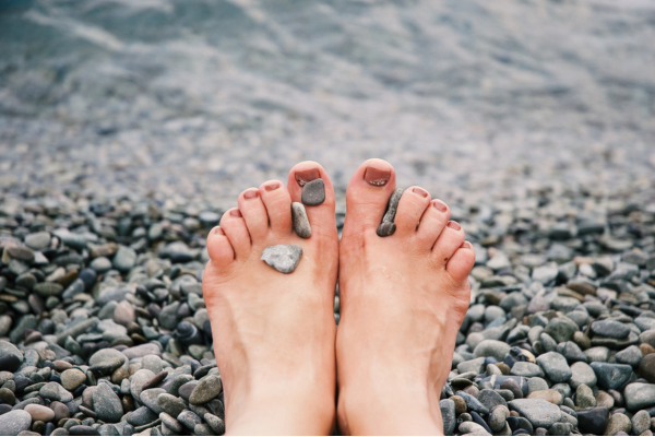 Clear Healthy Toenails Following Ingrown Toenail Removal A view of healthy, well-trimmed toenails on clean feet resting on a pebble beach, symbolizing successful recovery and foot health.