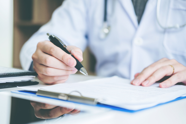 Podiatrist in white coat with stethoscope writing notes on a patient treatment plan clipboard during a gout evaluation appointment at Foot & Ankle Centers of New Jersey